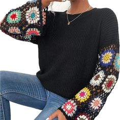 a woman sitting on a chair with her hand in her hair and wearing a black sweater with multicolored crochet sleeves