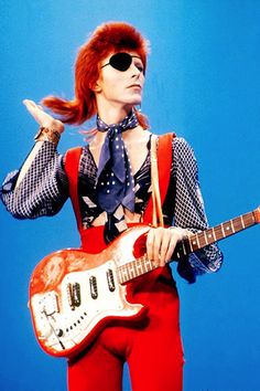 a man in red pants and sunglasses holding an electric guitar with his right hand up