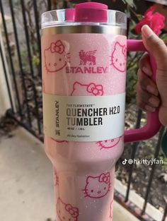 a person holding a pink hello kitty tumbler in front of a fence with flowers