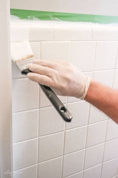 a person with gloves on holding a paint brush in front of a white tiled wall