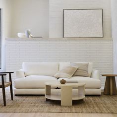 a living room with white couches and tables in front of a painting on the wall