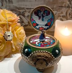 an ornate jewelry box sitting next to a candle and flowers on a white tablecloth