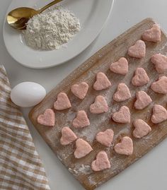 heart shaped cookies are on a cutting board next to a plate with eggs and flour