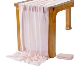 a wooden bench with pink fabric draped over it and a white blanket on the ground