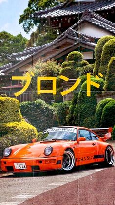 an orange sports car parked in front of a japanese house with trees and bushes behind it