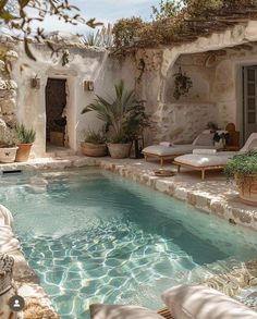 an outdoor swimming pool with lounge chairs and potted plants next to it, surrounded by stone walls