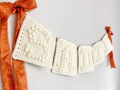 a white crochet banner hanging on a wall with an orange ribbon around it