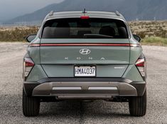 the back end of a gray suv parked in a parking lot with mountains in the background