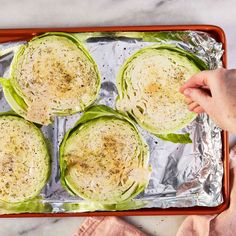 four lettuce wrapped in foil on top of a baking sheet with someone's hand