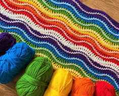 several balls of yarn sitting on top of a wooden floor next to a crochet afghan