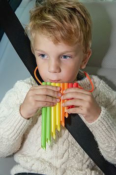 a little boy sitting in a car seat chewing on an item with colored sticks attached to it