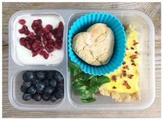 a plastic container filled with food on top of a wooden table next to blueberries and raspberries