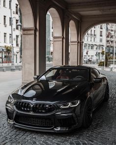 a black bmw car parked in front of a building on a cobblestone street