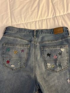 a pair of blue jeans with colorful embroidered stars and bows on the back, sitting on top of a bed
