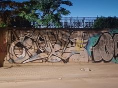 a wall covered in graffiti next to a tree