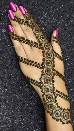 a woman's hand with henna tattoos on it and pink nail polishes