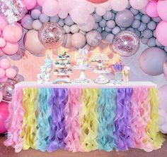 a table topped with lots of balloons next to a wall covered in pink, yellow and purple