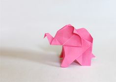 an origami elephant made out of pink paper on a white surface with its trunk curled up