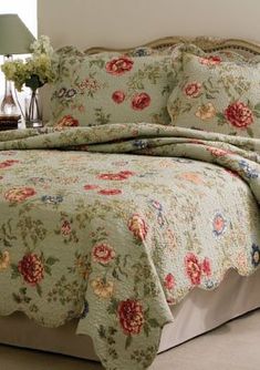 a bed with a flowered comforter and pillows on it in a room next to a lamp