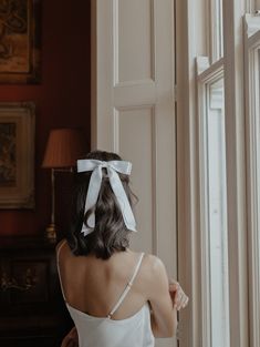 the back of a woman's head wearing a white bow in front of a window