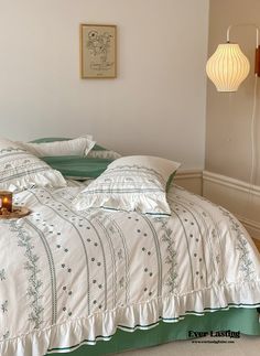 a bed with white and green comforter next to a wall light in a bedroom