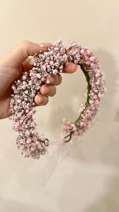 a hand holding a pink flower wreath with small white flowers on the top and bottom