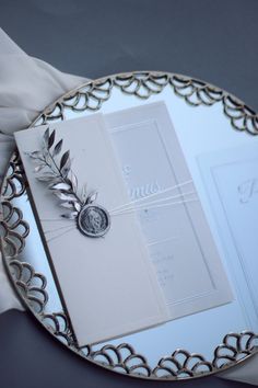 the wedding card is placed on top of the silver plate with an embellishment