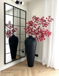 two black vases with red flowers sit in front of a mirror on the floor