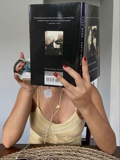 a woman sitting at a table reading a book and listening to headphones on her ears