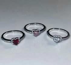 three heart shaped rings sitting on top of a white table next to two other rings