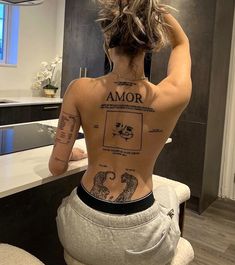 a woman with tattoos on her back sitting in front of a mirror