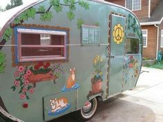 an old trailer painted with cats and flowers on it's side in front of a house