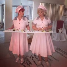 two women in pink dresses are holding a tray with desserts on it while standing next to each other