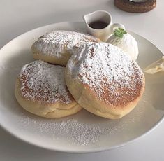 three powdered sugar covered pastries on a white plate next to a cup of coffee