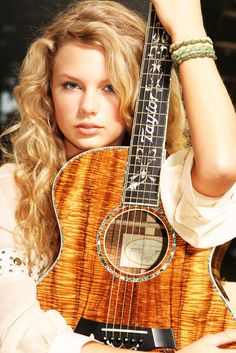 a woman is holding an acoustic guitar in her right hand and posing for the camera