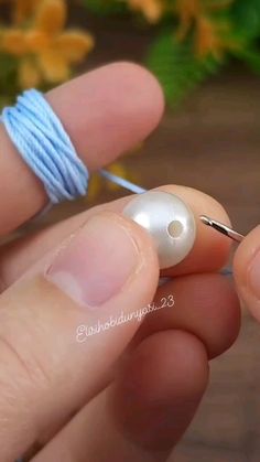 a person holding a thread and needle in their left hand, with a white pearl bead on it