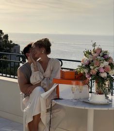 a man and woman sitting on a bench next to each other in front of the ocean