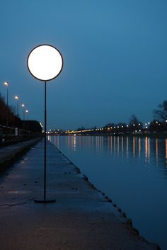 a street light sitting on the side of a body of water next to a sidewalk