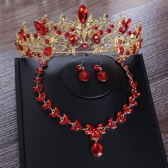 a red and gold tiara with matching jewelry set on a black display case in front of a wooden table