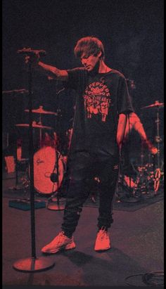 a young man standing next to a microphone on top of a stage in front of drums