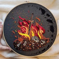 someone is holding up a cross - stitch art piece with flames and skulls on it