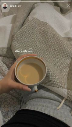 a person holding a cup of coffee on top of a bed next to a blanket