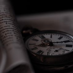 a pocket watch sitting on top of an open book with roman numerals in the background