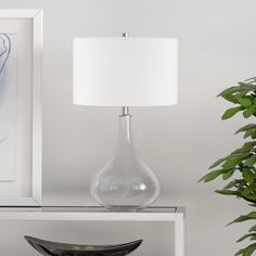 a glass vase sitting on top of a table next to a lamp and framed artwork