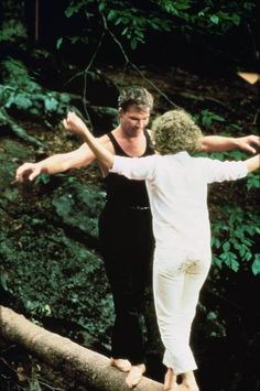 two people standing on a fallen tree in the woods, one holding his arms out