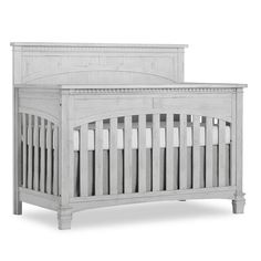 a baby crib that is white and has wood trimmings on the sides