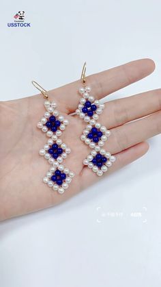 a person's hand holding two pairs of blue and white beaded earrings