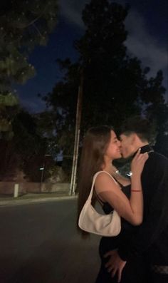 a man and woman are kissing in the street at night with trees in the background