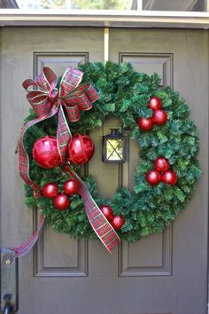 a christmas wreath on the front door of a house with red and green ornaments hanging from it