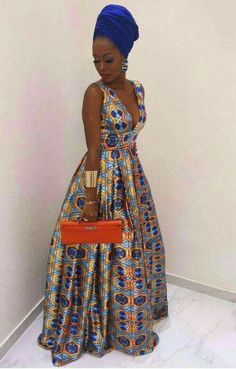 a woman in a blue and yellow dress holding an orange purse standing next to a wall